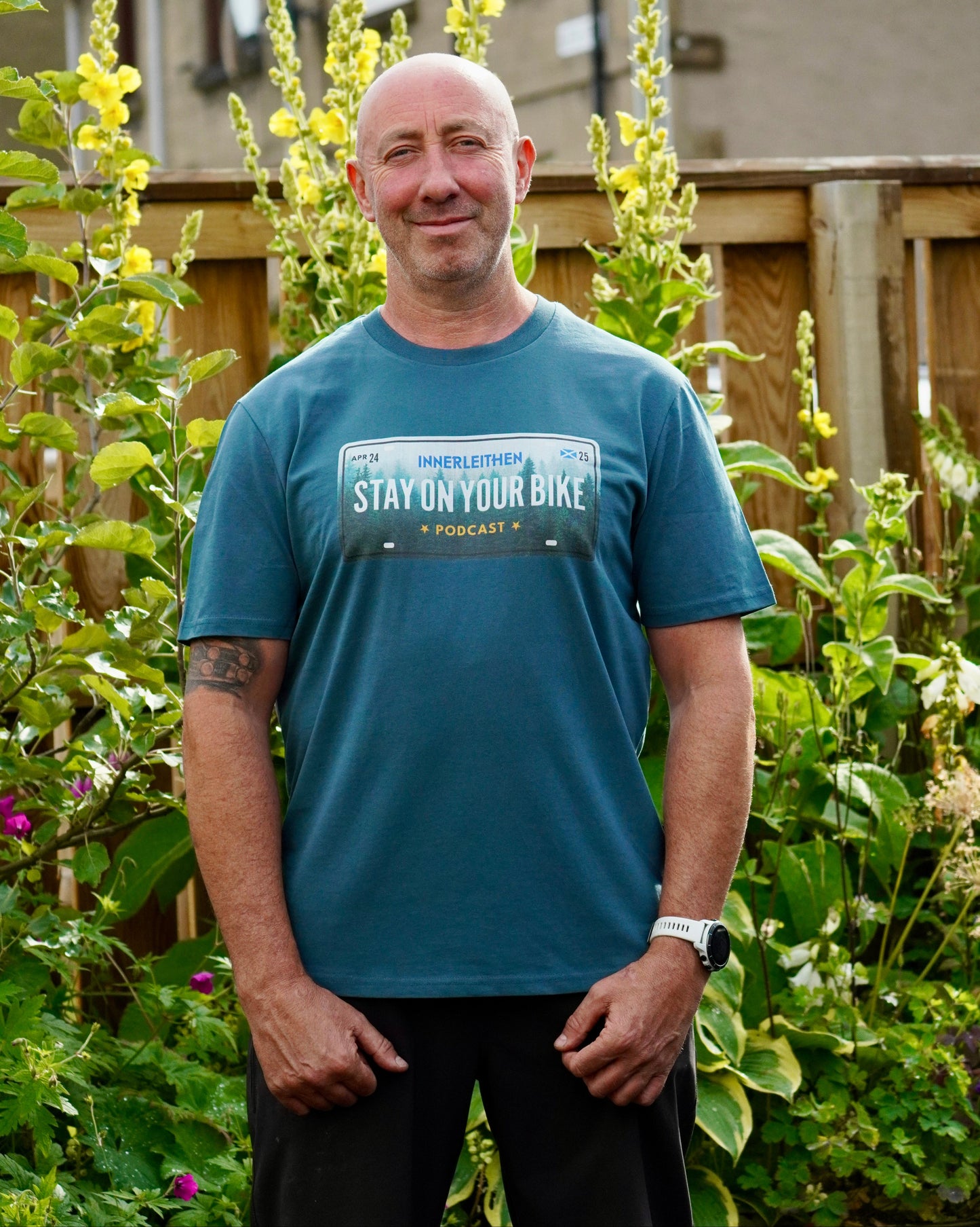 Nigel Page wearing Blue short-sleeve Into The Woods T-Shirt made from 100% organic cotton, featuring 'Stay on Your Bike' and Innerleithen print – podcast merch and mountain biking souvenir from the Tweed Valley