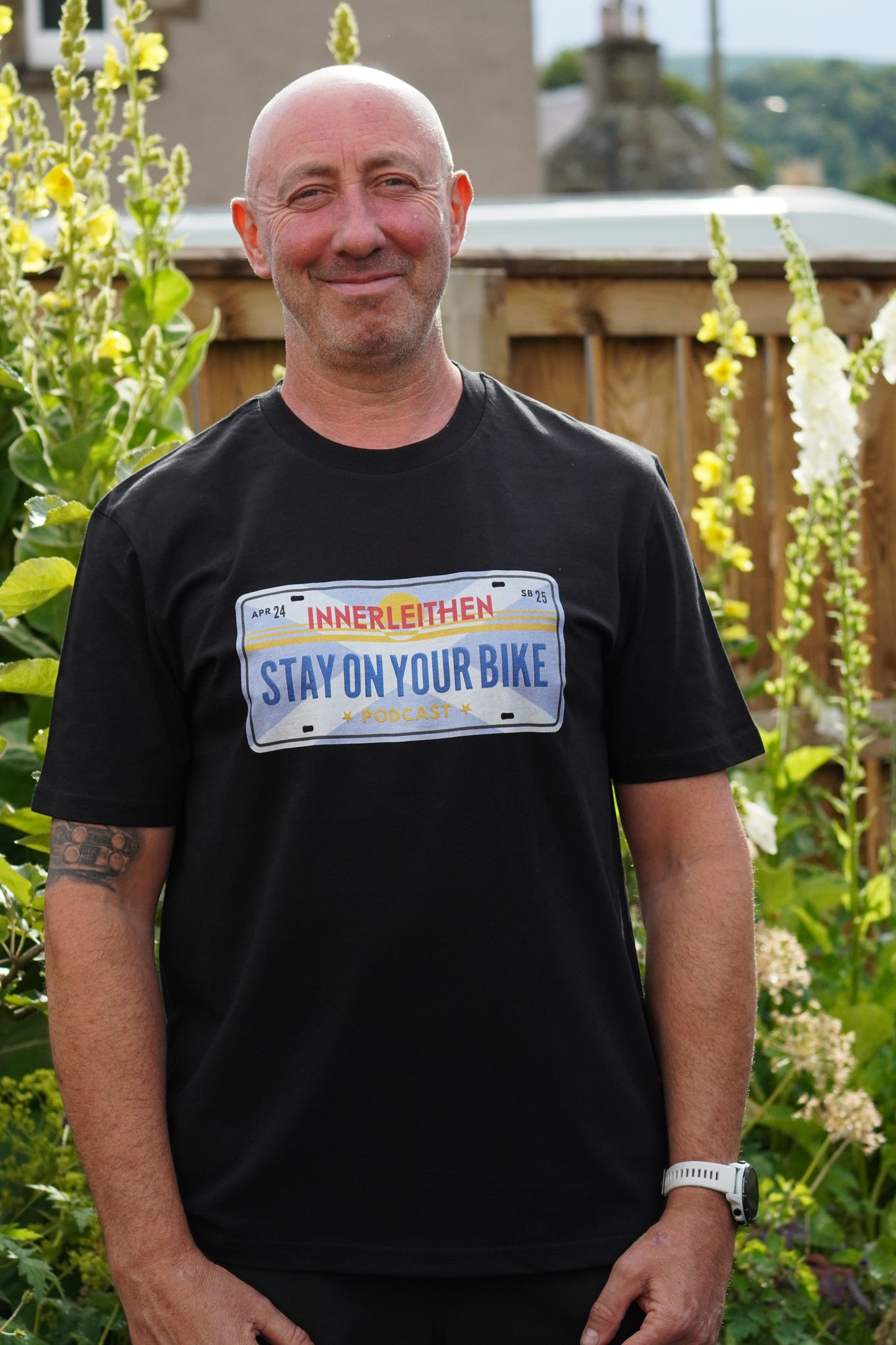 Nigel Page wearing black Loam Days T-shirt made from 100% organic cotton, featuring Californian style licence plate design with 'Stay on Your Bike' and 'Innerleithen' text – mountain biking merch and souvenir from Tweed Valley, inspired by Stay on Your Bike podcast