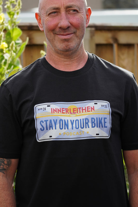 Close-up of Nigel Page wearing Californian style licence plate design on black Loam Days T-shirt made from 100% organic cotton, featuring 'Stay on Your Bike' and 'Innerleithen' text with horizon graphic – mountain biking merch and souvenir from Tweed Valley, inspired by Stay on Your Bike podcast