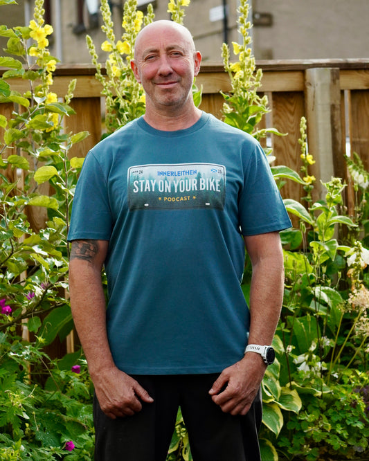Nigel Page wearing Blue short-sleeve Into The Woods T-Shirt made from 100% organic cotton, featuring 'Stay on Your Bike' and Innerleithen print – podcast merch and mountain biking souvenir from the Tweed Valley