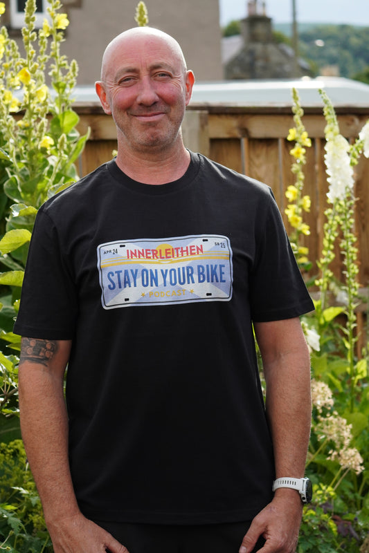 Nigel Page wearing black Loam Days T-shirt made from 100% organic cotton, featuring Californian style licence plate design with 'Stay on Your Bike' and 'Innerleithen' text – mountain biking merch and souvenir from Tweed Valley, inspired by Stay on Your Bike podcast